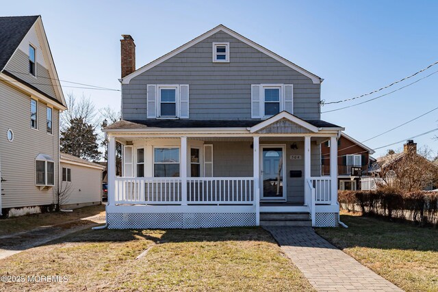 view of front of property with covered porch, a chimney, and a front yard