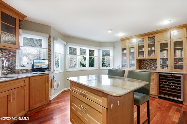 kitchen with a breakfast bar, backsplash, a sink, light stone countertops, and beverage cooler