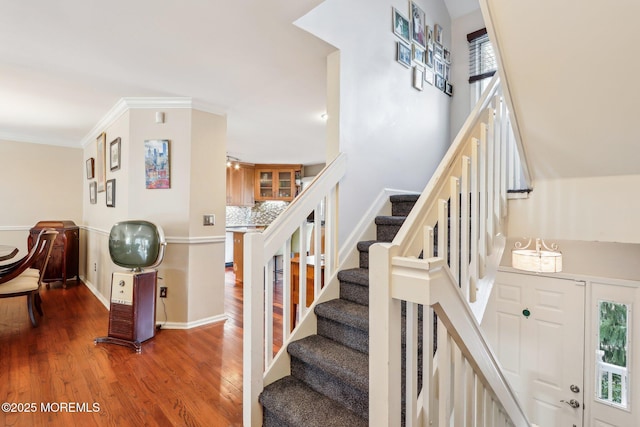 staircase with ornamental molding, baseboards, and wood finished floors