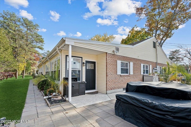 back of property featuring brick siding, a patio, and a lawn