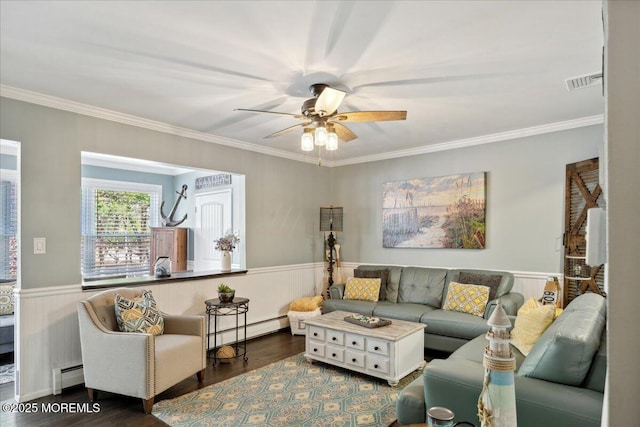 living room featuring a baseboard heating unit, dark wood-type flooring, visible vents, a ceiling fan, and wainscoting