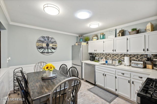 kitchen with wainscoting, ornamental molding, light countertops, stainless steel appliances, and a sink