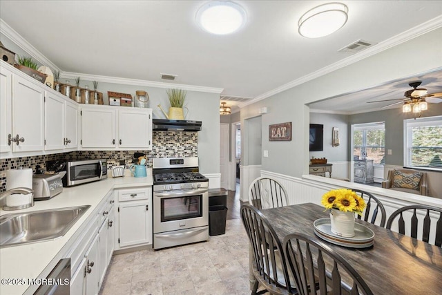 kitchen featuring stainless steel appliances, light countertops, wainscoting, white cabinetry, and under cabinet range hood