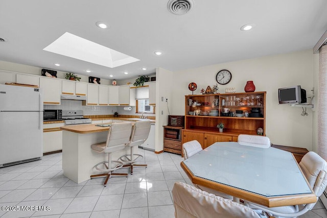 kitchen with under cabinet range hood, white appliances, a skylight, visible vents, and white cabinets