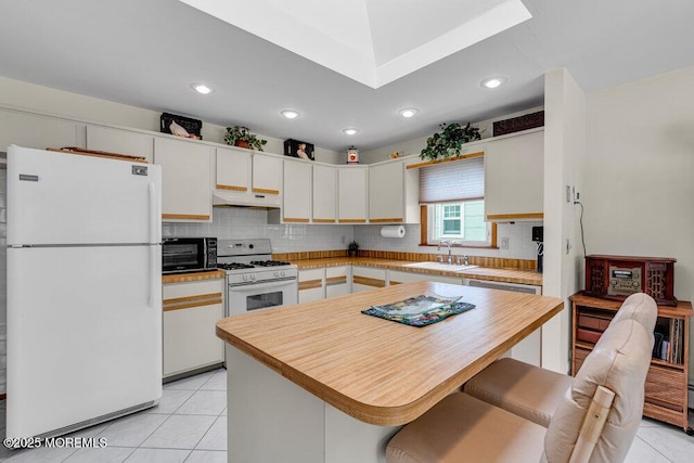 kitchen featuring light tile patterned floors, under cabinet range hood, white appliances, a sink, and tasteful backsplash