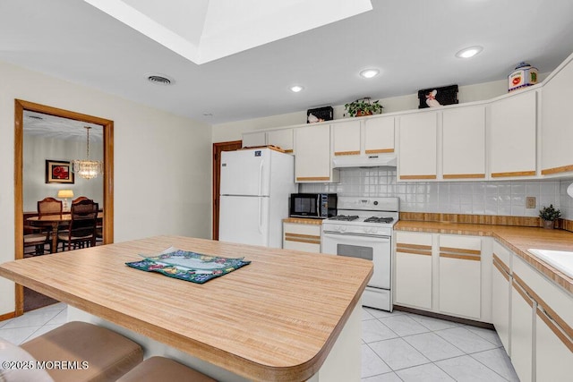 kitchen with light countertops, visible vents, backsplash, white appliances, and under cabinet range hood