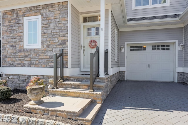 entrance to property with decorative driveway, stone siding, a shingled roof, and an attached garage