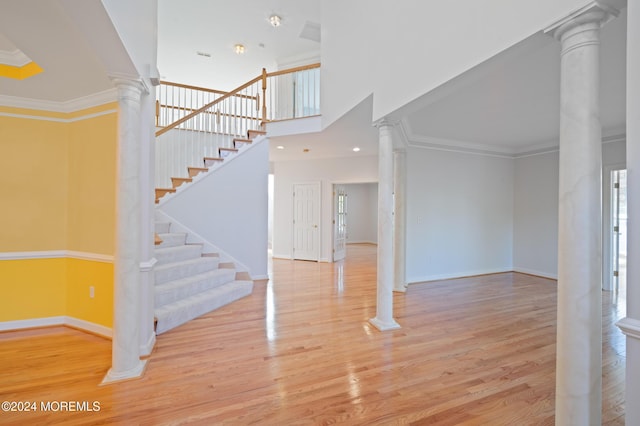 interior space featuring baseboards, wood finished floors, decorative columns, and crown molding