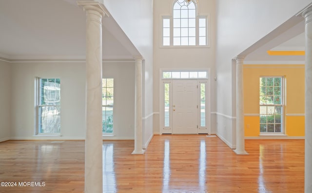 foyer entrance featuring light wood-style floors, decorative columns, ornamental molding, and a wealth of natural light