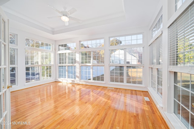 unfurnished sunroom featuring a ceiling fan, a tray ceiling, and a wealth of natural light