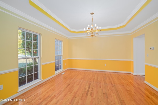 spare room with baseboards, wood finished floors, a tray ceiling, crown molding, and a notable chandelier