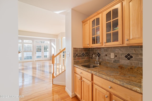 kitchen featuring light wood-style flooring, glass insert cabinets, a sink, stone counters, and backsplash