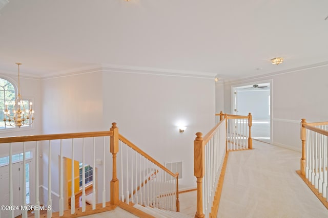 hallway featuring light carpet, visible vents, crown molding, an upstairs landing, and a chandelier