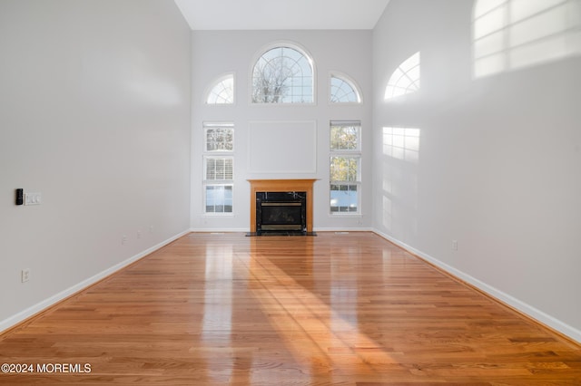 unfurnished living room with a high ceiling, light wood finished floors, a fireplace, and baseboards