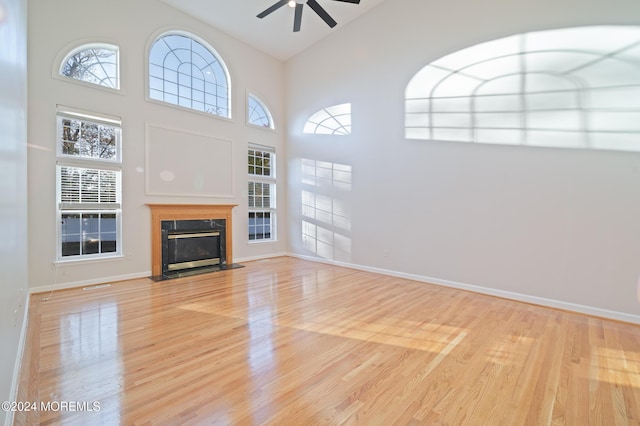 unfurnished living room with ceiling fan, light wood finished floors, a fireplace, and baseboards