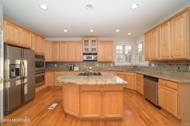 kitchen with a sink, stainless steel appliances, a kitchen island, and light brown cabinets