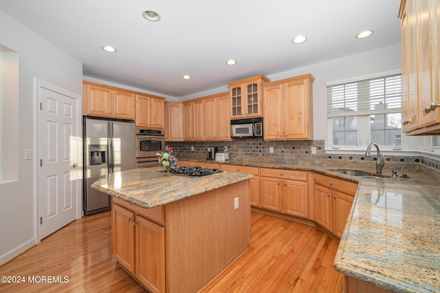 kitchen with decorative backsplash, a kitchen island, stainless steel appliances, light wood-type flooring, and a sink