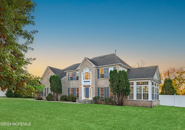 view of front of house with fence, a lawn, and brick siding