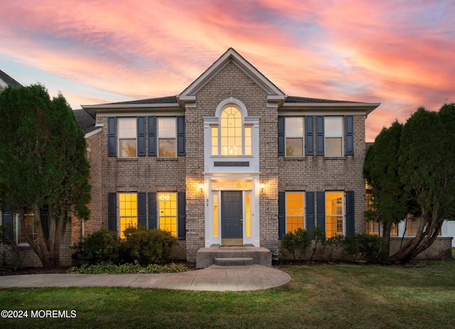 colonial inspired home featuring a lawn and brick siding