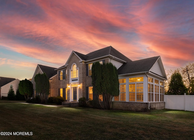 view of front of house with a front yard, a sunroom, brick siding, and fence