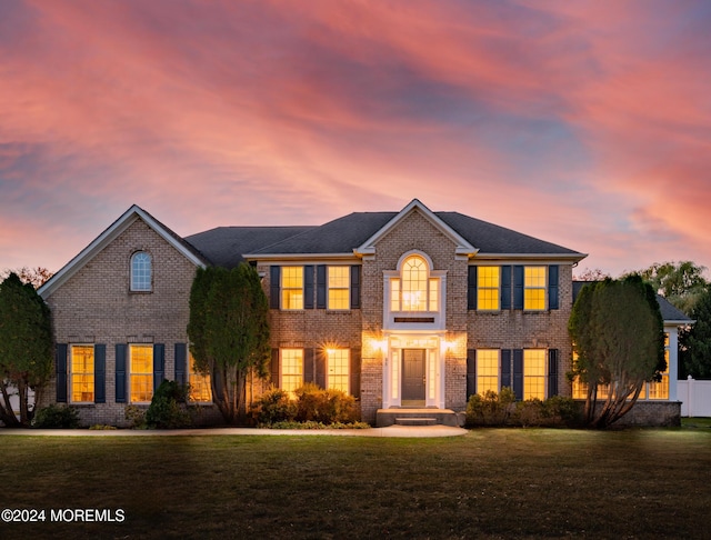 colonial inspired home with fence, a lawn, and brick siding