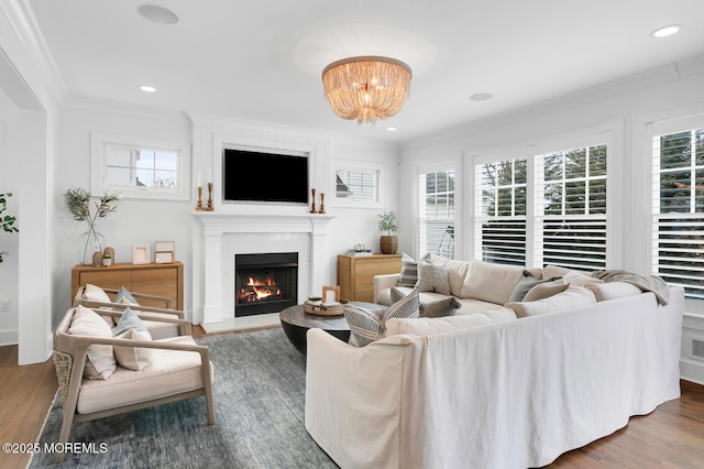 living area with recessed lighting, wood finished floors, a lit fireplace, and ornamental molding