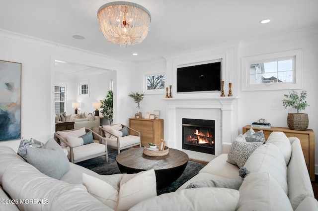 living room with crown molding, recessed lighting, a chandelier, and a lit fireplace