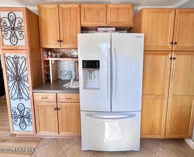 kitchen with white fridge with ice dispenser, dark countertops, and light tile patterned floors