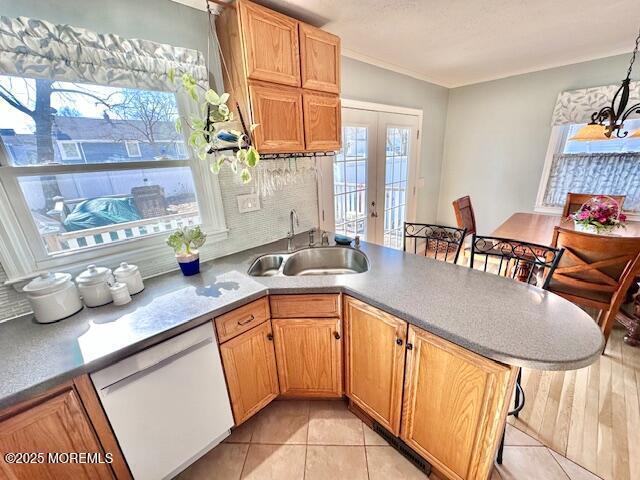 kitchen featuring a chandelier, white dishwasher, a peninsula, a sink, and french doors