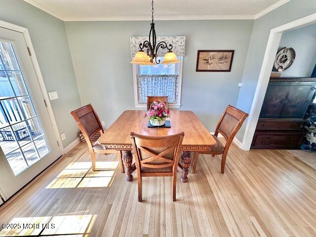 dining room with a chandelier, ornamental molding, light wood-type flooring, and baseboards