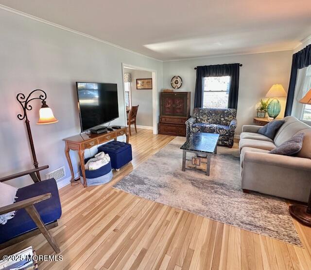 living area featuring baseboards, wood finished floors, visible vents, and crown molding