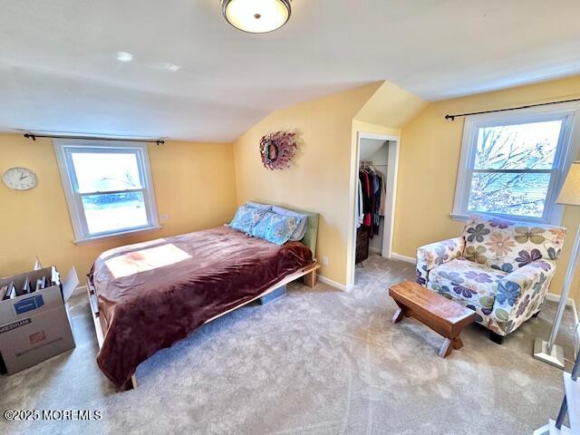 bedroom featuring a walk in closet, a closet, carpet flooring, vaulted ceiling, and baseboards