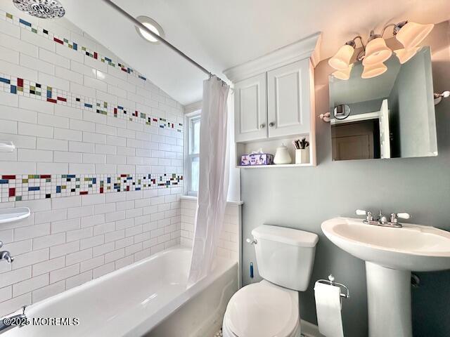 full bath with toilet, a sink, vaulted ceiling, and shower / bath combination with curtain