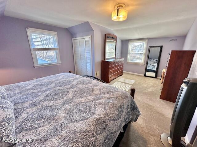 bedroom featuring light carpet, vaulted ceiling, a closet, and baseboards