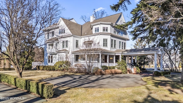 view of front of house featuring covered porch, driveway, a chimney, and a front lawn