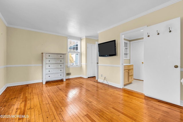 empty room with ornamental molding, light wood-type flooring, visible vents, and baseboards