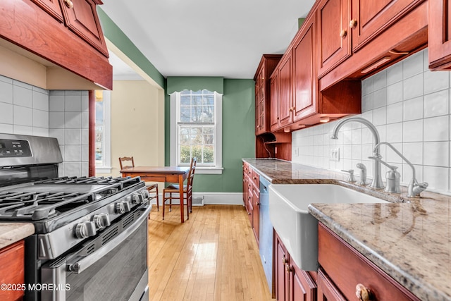 kitchen with baseboards, appliances with stainless steel finishes, light wood-type flooring, backsplash, and light stone countertops