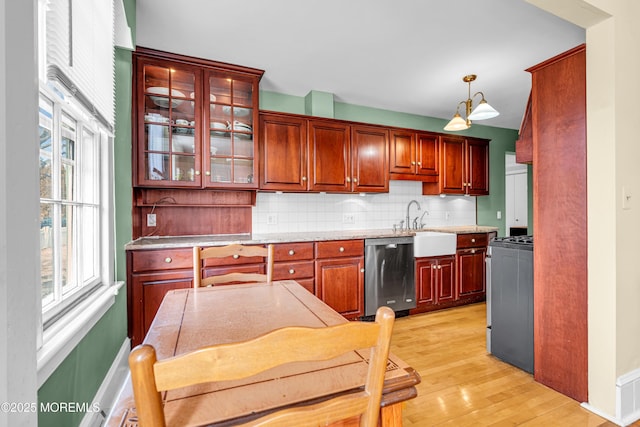 kitchen with light wood-style flooring, stainless steel appliances, a sink, backsplash, and decorative light fixtures