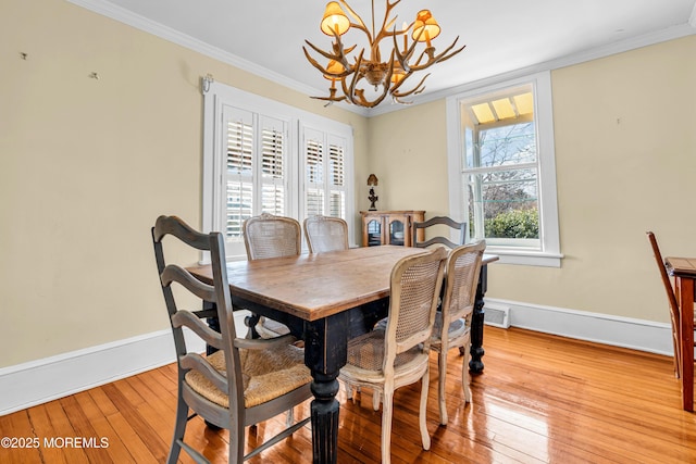 dining space with light wood-type flooring, a notable chandelier, crown molding, and baseboards