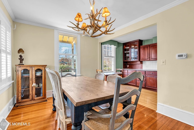 dining area featuring a chandelier, light wood-type flooring, crown molding, and baseboards