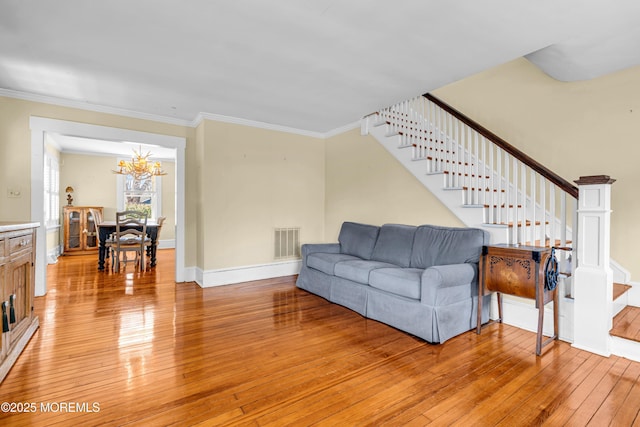 living room featuring light wood finished floors, visible vents, baseboards, ornamental molding, and stairs