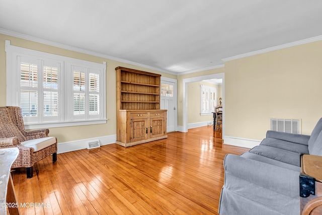 living room with light wood finished floors, visible vents, and crown molding