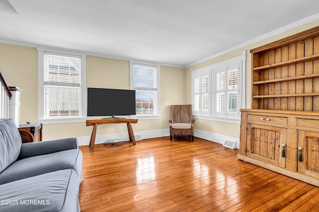 living room featuring light wood-type flooring, visible vents, baseboards, and crown molding