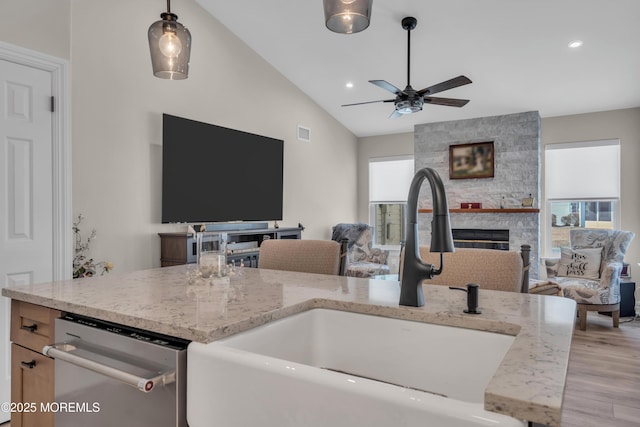 interior space featuring lofted ceiling, a stone fireplace, a sink, open floor plan, and stainless steel dishwasher