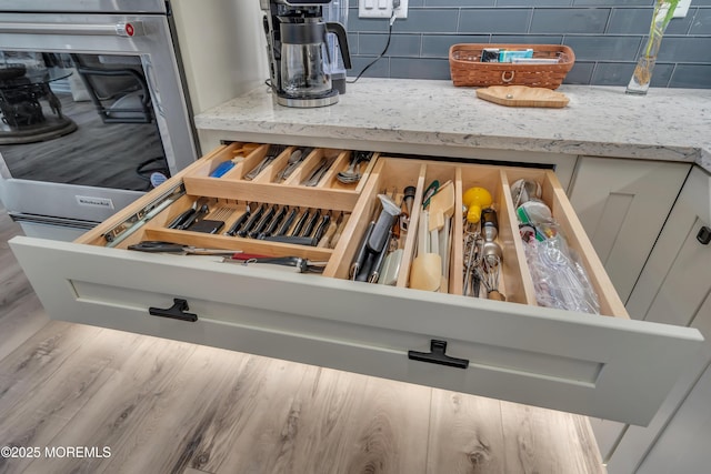 details featuring wood finished floors, stainless steel oven, backsplash, and light stone countertops