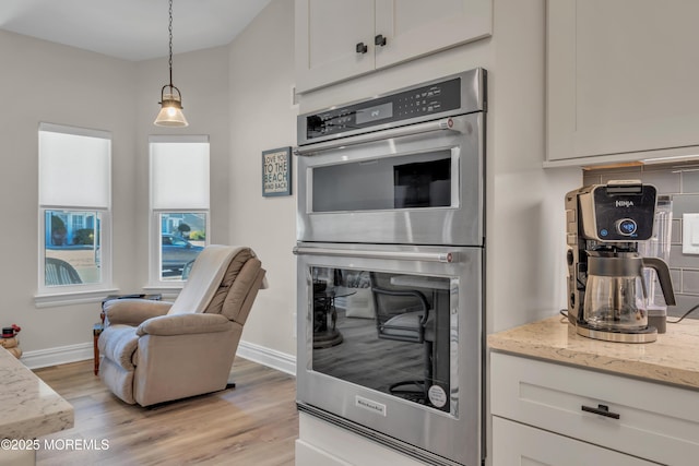 kitchen with light wood-type flooring, stainless steel double oven, baseboards, and light stone counters