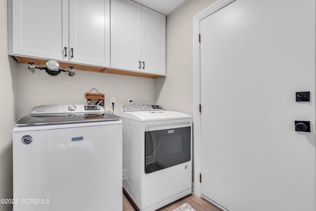 laundry area featuring light wood-type flooring, cabinet space, and washing machine and clothes dryer