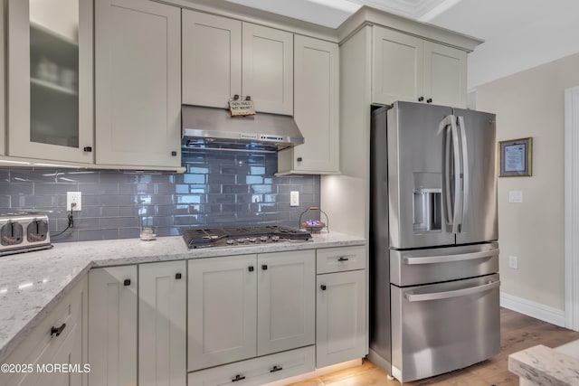 kitchen featuring range hood, stainless steel appliances, backsplash, light wood-style floors, and light stone countertops