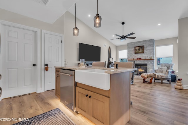 kitchen featuring a stone fireplace, a kitchen island with sink, open floor plan, stainless steel dishwasher, and light wood finished floors