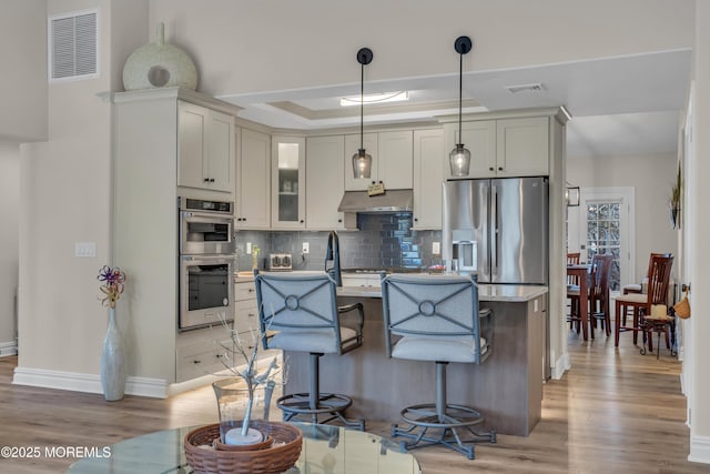 kitchen featuring stainless steel appliances, light wood-style floors, visible vents, and decorative backsplash